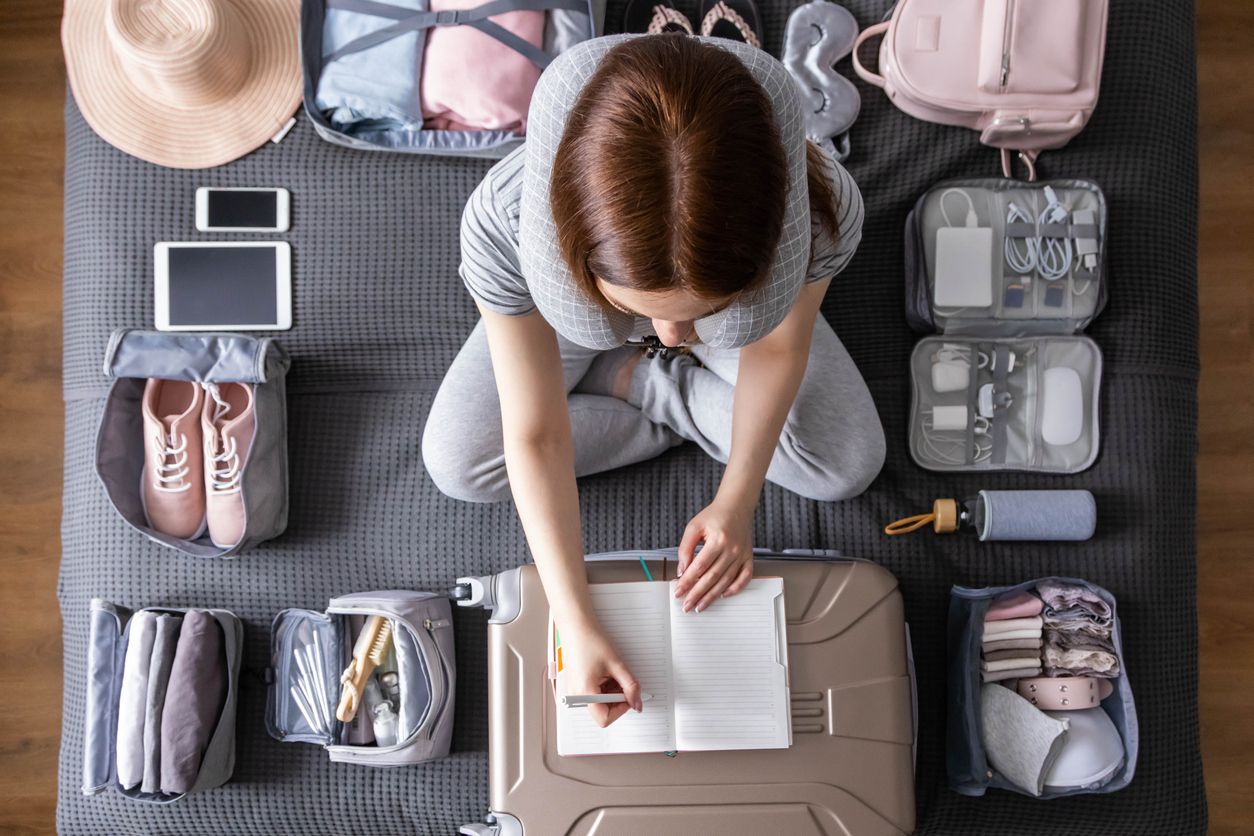 Woman packing suitcase to vacation writing paper list getting ready to travel trip