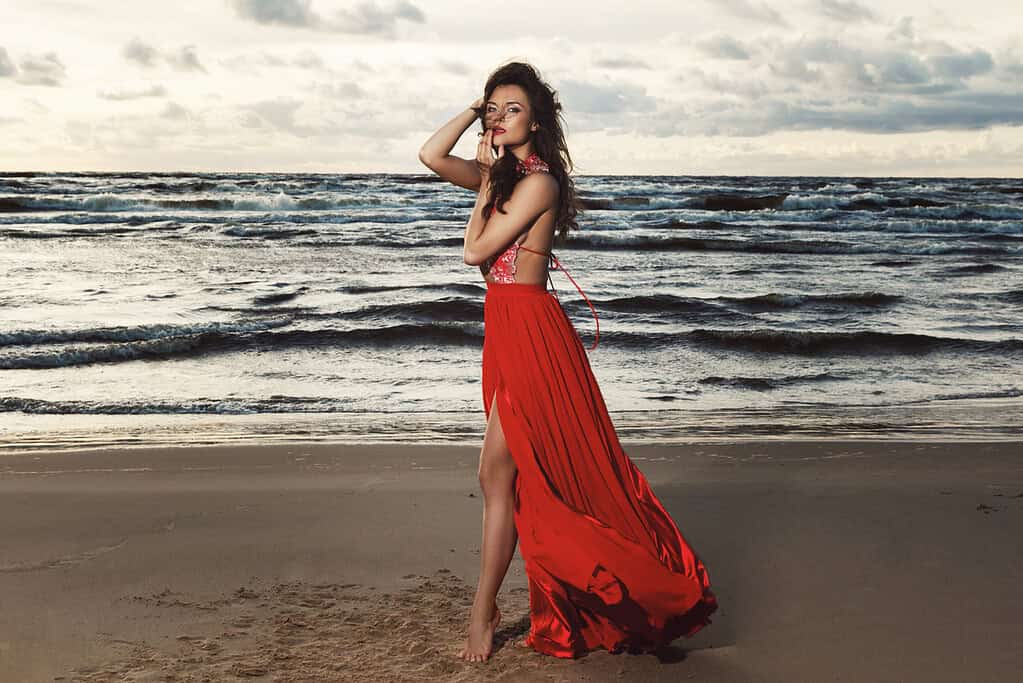 Stunning woman wearing beautiful red dress on the beach during sunset time - What to wear to a wedding in Ibiza.